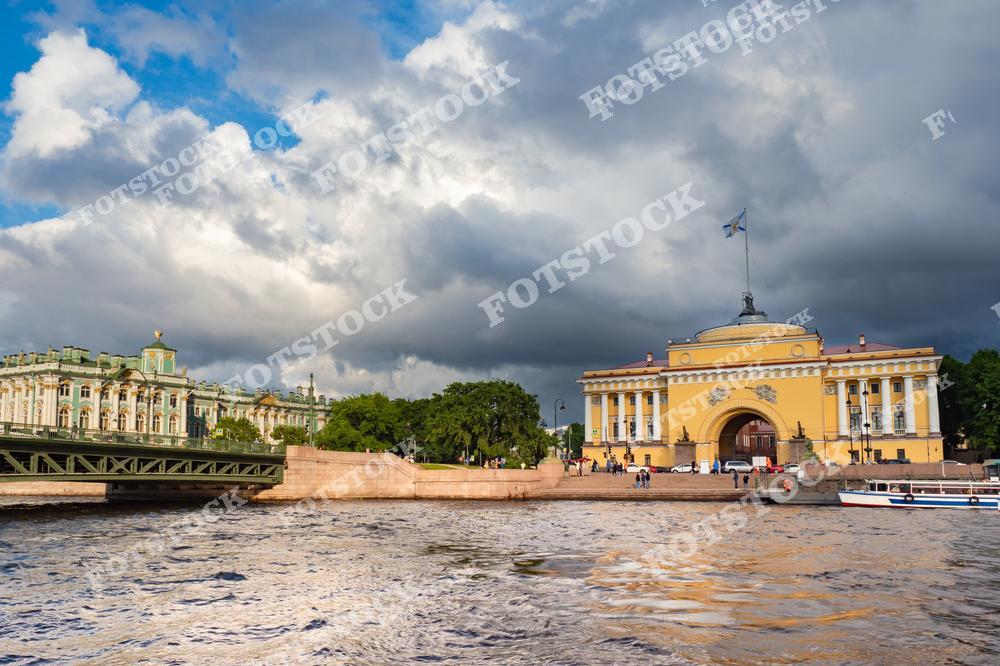 На фотографии запечатлены Зимний дворец и здание Адмиралтейства, расположенные на набережной реки Невы в Санкт-Петербурге. Эти величественные строения, являющиеся символами российской архитектуры, привлекают внимание своей красотой и исторической значимостью. Летний день с облачным небом добавляет драматичности пейзажу.